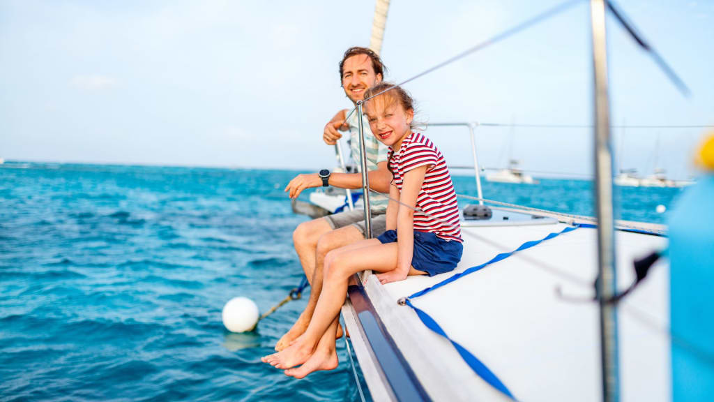 A man and a girl sit on the edge of a boat in the clear, blue waters near one of the most beautiful beaches in Costa Rica under a sunny sky.